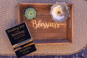 The book, Finding Joy in the Morning by Jacquelyn Lynn, on a table with a tray that has the word Blessings written on it.