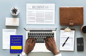 A desktop with laptop, clipboard, newspaper, and a copy of Christian Business Almanac