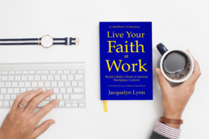 The book, Live Your Faith at Work, on a desk with a keyboard and a hand hold a cup of coffee